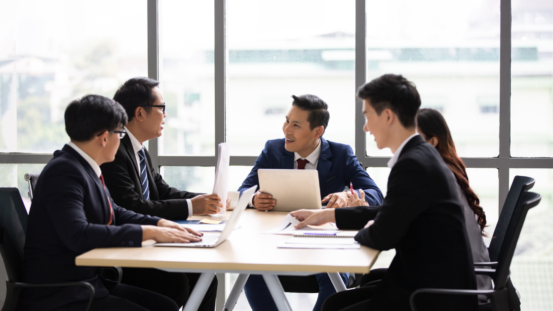 A group of Singaporean executives engaged in a discussion about health screening SG in a modern office setting
