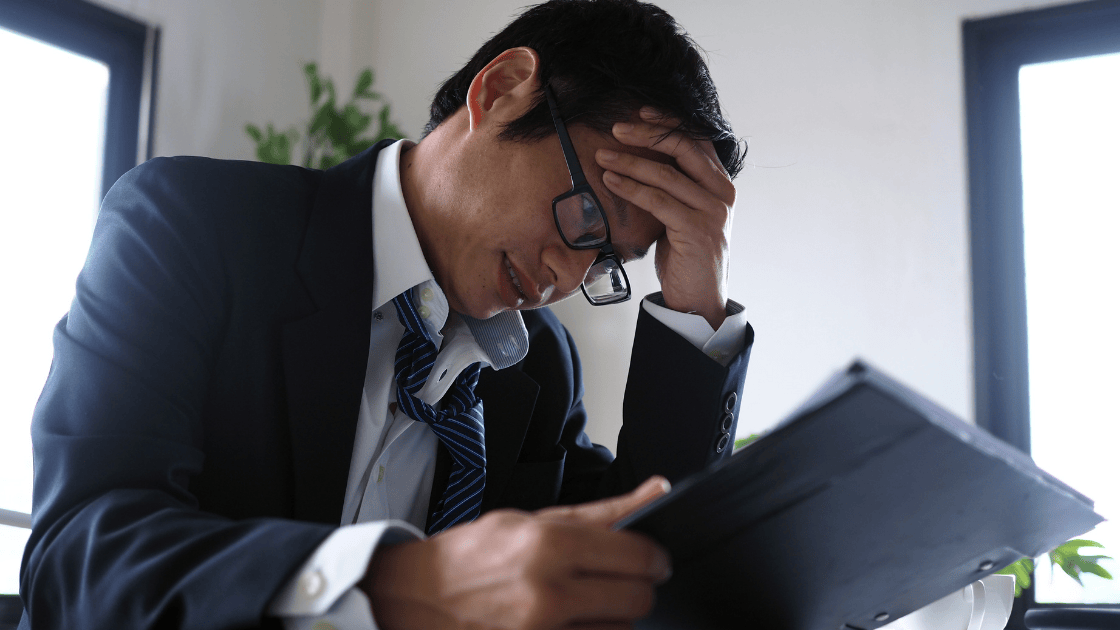 A stressed corporate worker holding their head in their hands, surrounded by paperwork and a glowing computer screen, symbolizing the mental health challenges of overwork. Explore health screening SG options to promote well-being