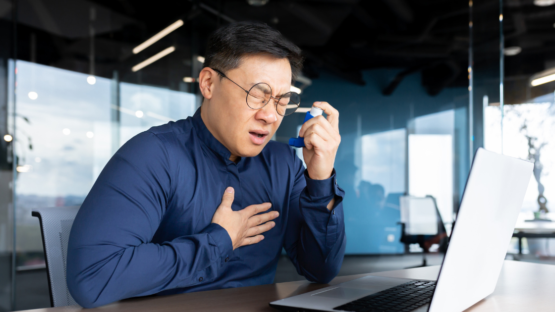 Man experiencing chest pain at work while holding an asthma inhaler – workplace asthma in Singapore