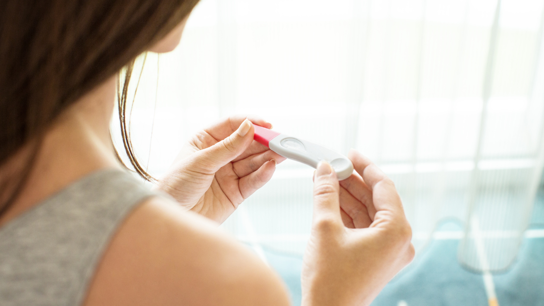 Woman holding pregnancy test strip considering health screening services in Singapore