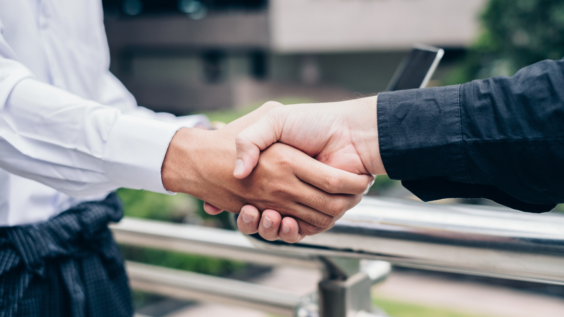 Two business professionals shaking hands in corporate office setting representing partnership in employee health screening programs