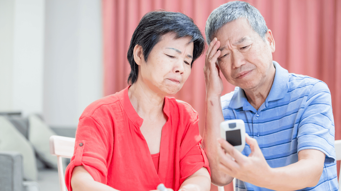 Senior couple in Singapore using handheld blood glucose meter for diabetes self-monitoring, demonstrating home health management