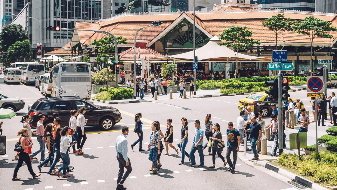 Young adults crossing busy street in Singapore business district representing urban professionals at risk for cancer requiring early screening