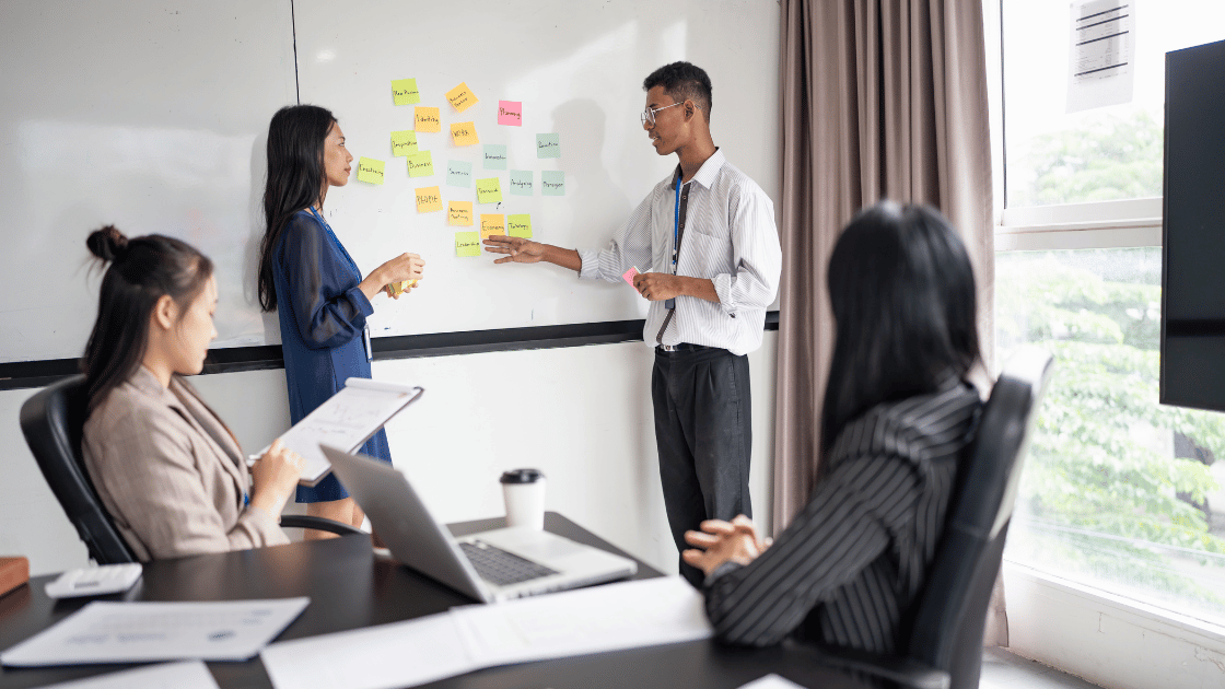 Four professional colleagues sitting around boardroom table during business meeting discussing employee wellness programs Singapore implementation strategy