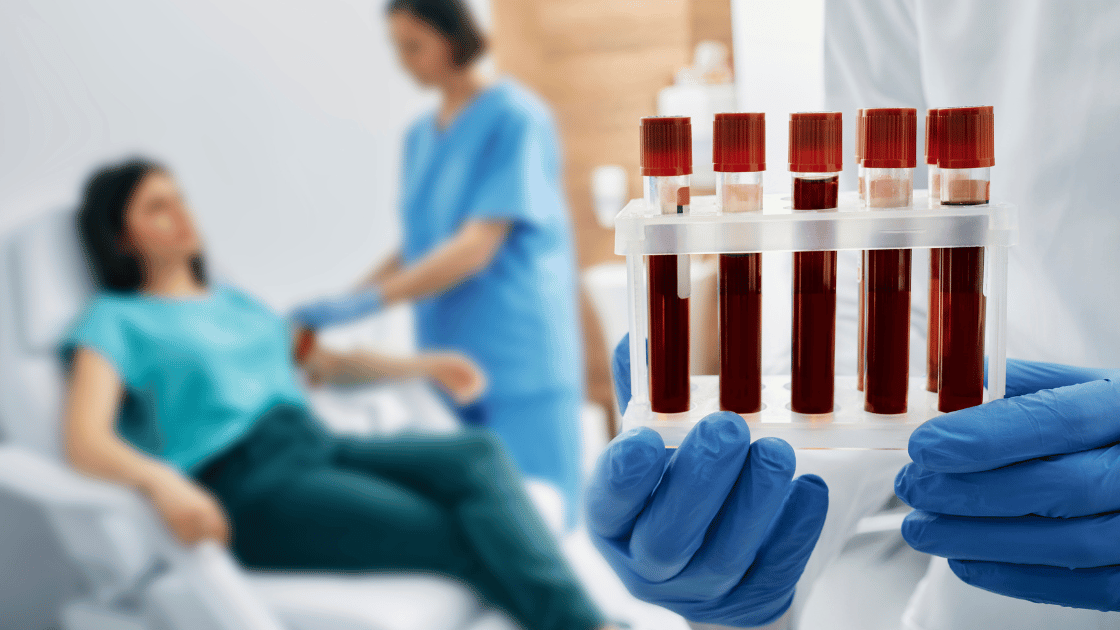 Blood test tubes in foreground with female patient having blood drawn by medical professional in background at Singapore health screening clinic