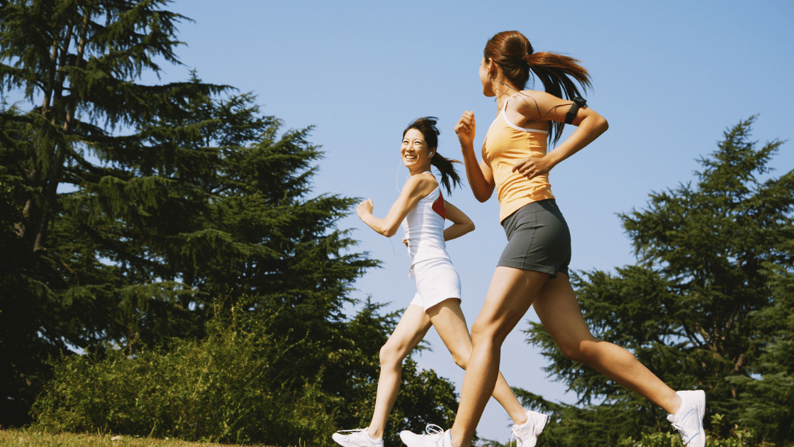 Two women jogging together in a Singapore park as part of healthy lifestyle habits for disease prevention