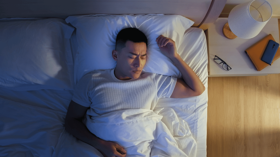 A frustrated man frowning while sleeping, representing the common sleep issues many Singaporeans face due to stress and work pressure