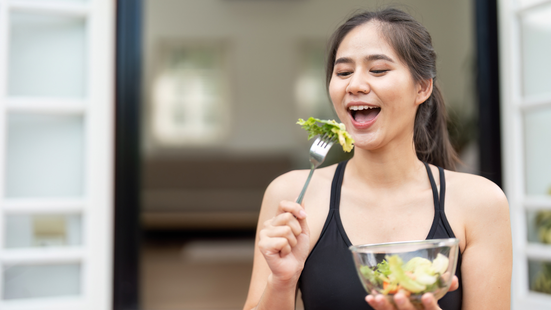 Young healthy woman holding a fork and a fresh green salad bowl, representing proper nutrition and healthy eating choices that improve health screening results