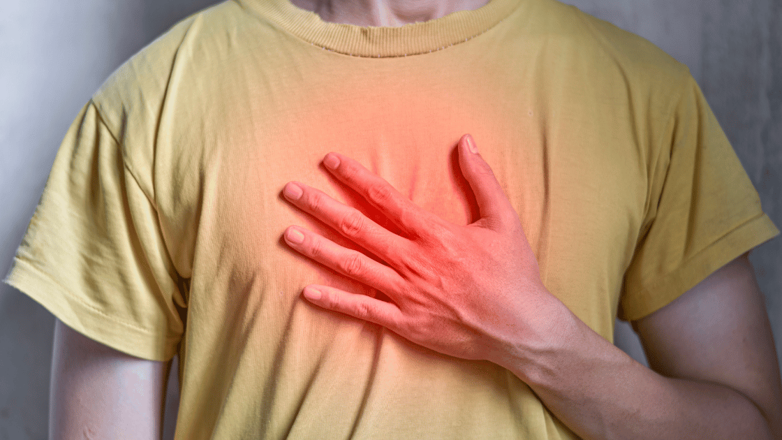 Asian man in casual clothing clutching his chest with concerned expression, illustrating heart attack symptoms and cardiovascular discomfort